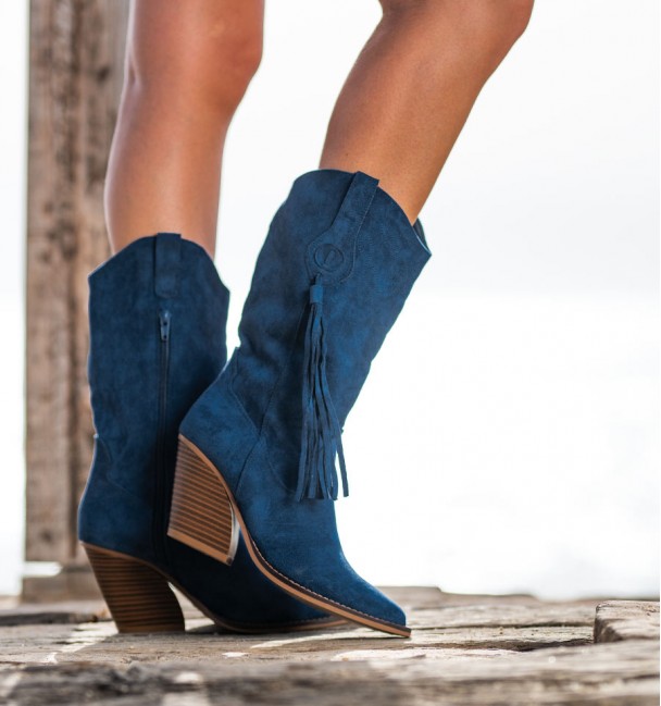Pernas femininas com botas de cowboy femininas na cor azul com salto cubano e o mar ao fundo.