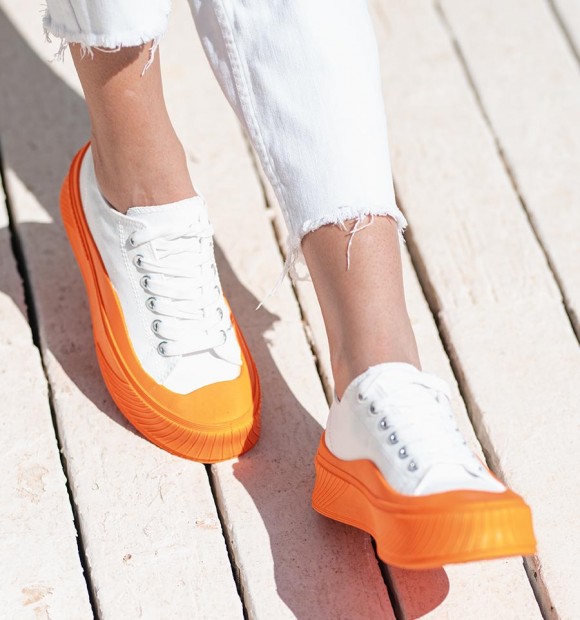 white canvas sneakers with thick soles and orange toe cap, lace up fastening