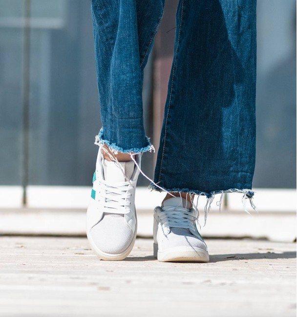 White vegan leather sneakers with two green lines and laces.
