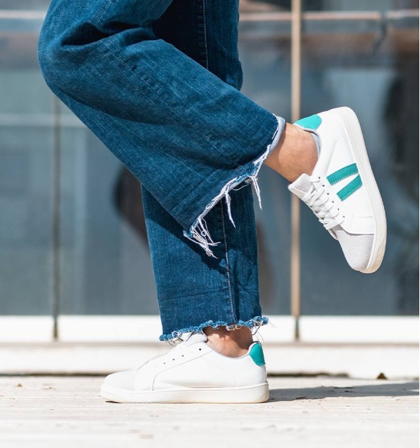 White vegan leather sneakers with two green lines and laces.