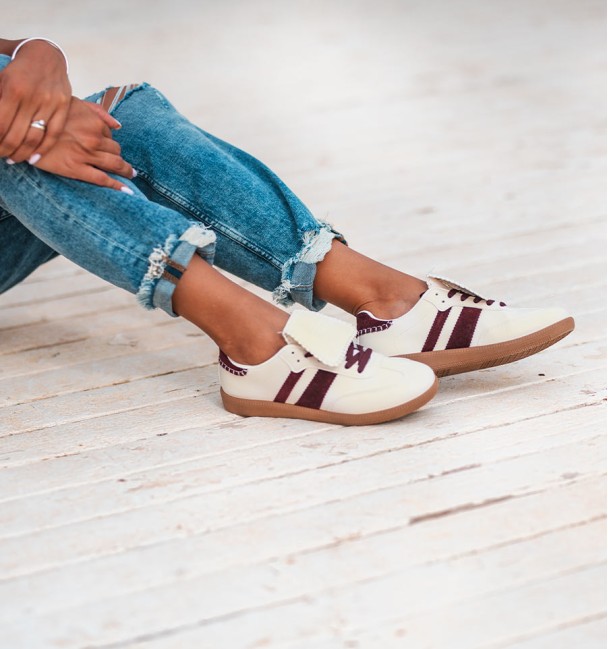 Zapatillas deportivas beige con lengüeta blanca . Dos rayas laterales burdeos y cordones también burdeos. Suela goma marrón