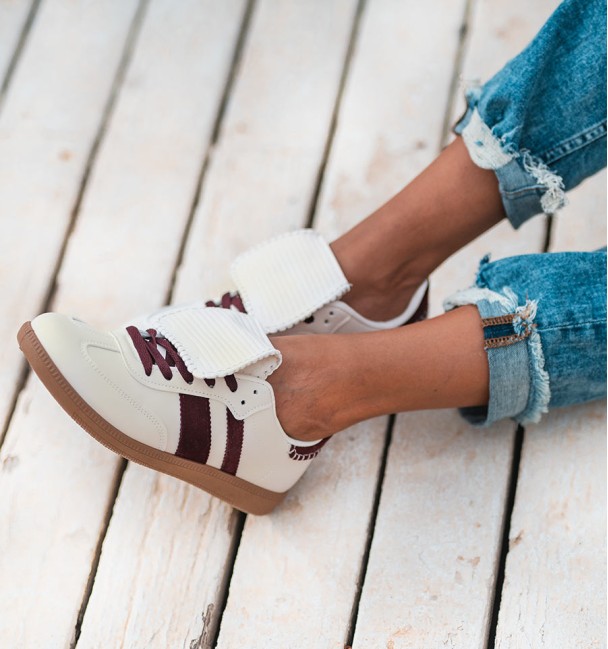 Zapatillas deportivas beige con lengüeta blanca . Dos rayas laterales burdeos y cordones también burdeos. Suela goma marrón