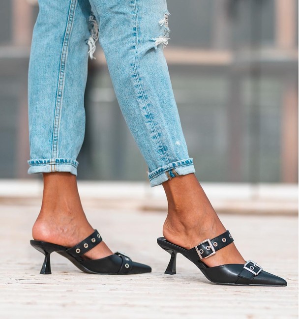 zapato destalonado en color negro con tacón bajo, tira con tachuelas y hebillas en empeine. Cuerina, animal free.
