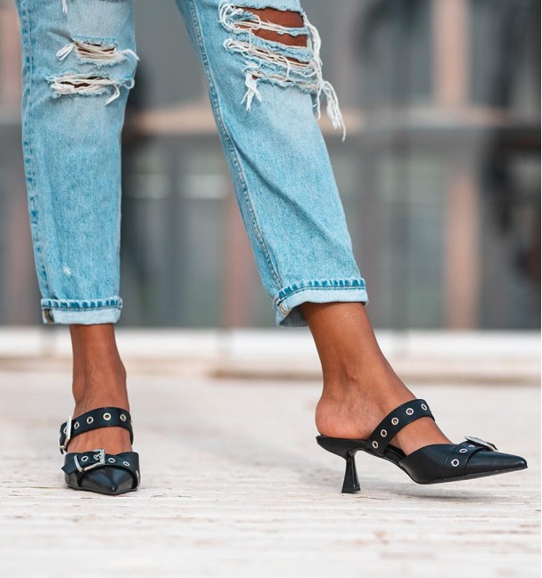 zapato destalonado en color negro con tacón bajo, tira con tachuelas y hebillas en empeine. Cuerina, animal free.
