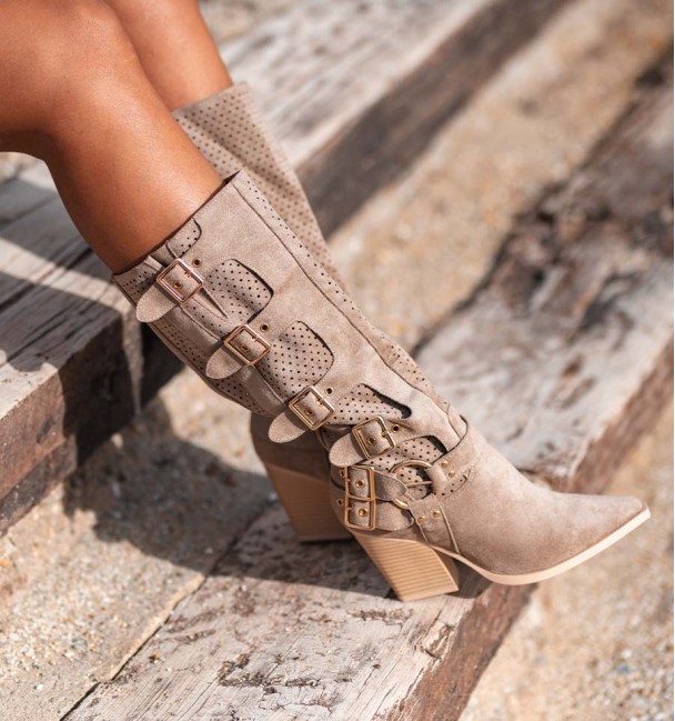Botas altas estilo cowboy com fivelas laterais e cano perfurado. Cor tostada (caqui) e salto. Têxteis