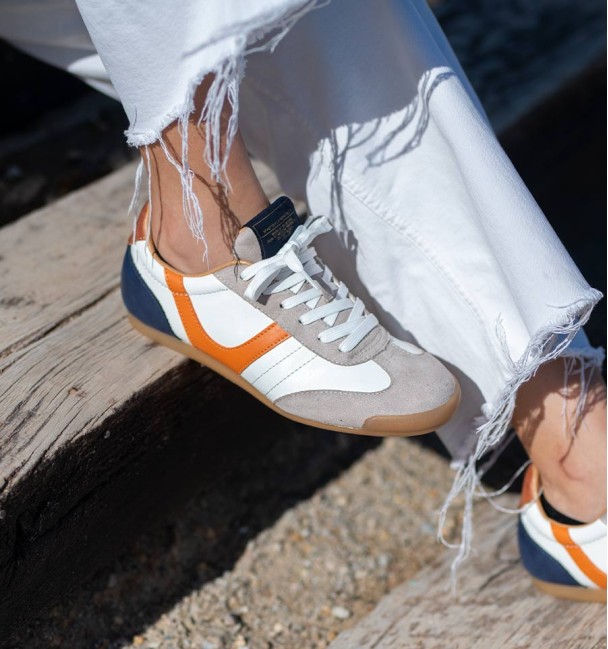 zapatillas deportivas blancas con puntera en serraje y detalle naranja y talón azul.