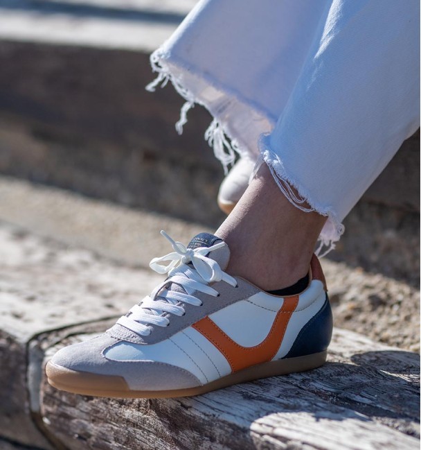 zapatillas deportivas blancas con puntera en serraje y detalle naranja y talón azul.