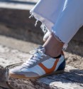 zapatillas deportivas blancas con puntera en serraje y detalle naranja y talón azul.